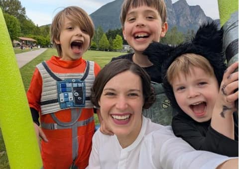 A smiling mother and three children in costumes taking a selfie in a park