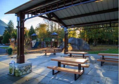 Picnic tables under a covered shelter beside a playground and boulders