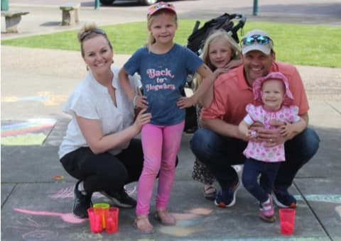 A family crouched together on a sidewalk decorated with chalk drawings